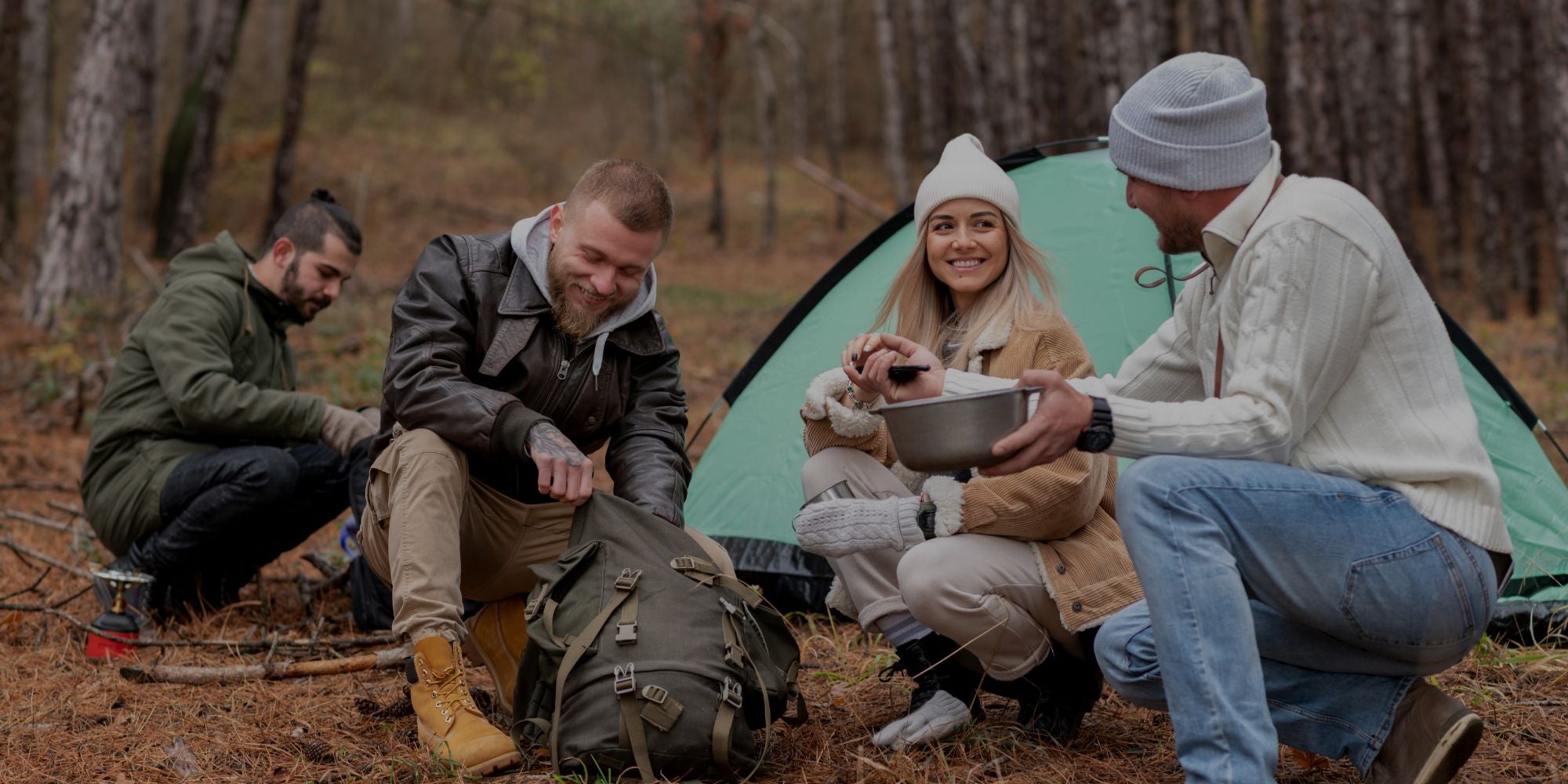 Group of people camping in a forest, sitting around a tent and preparing food.
